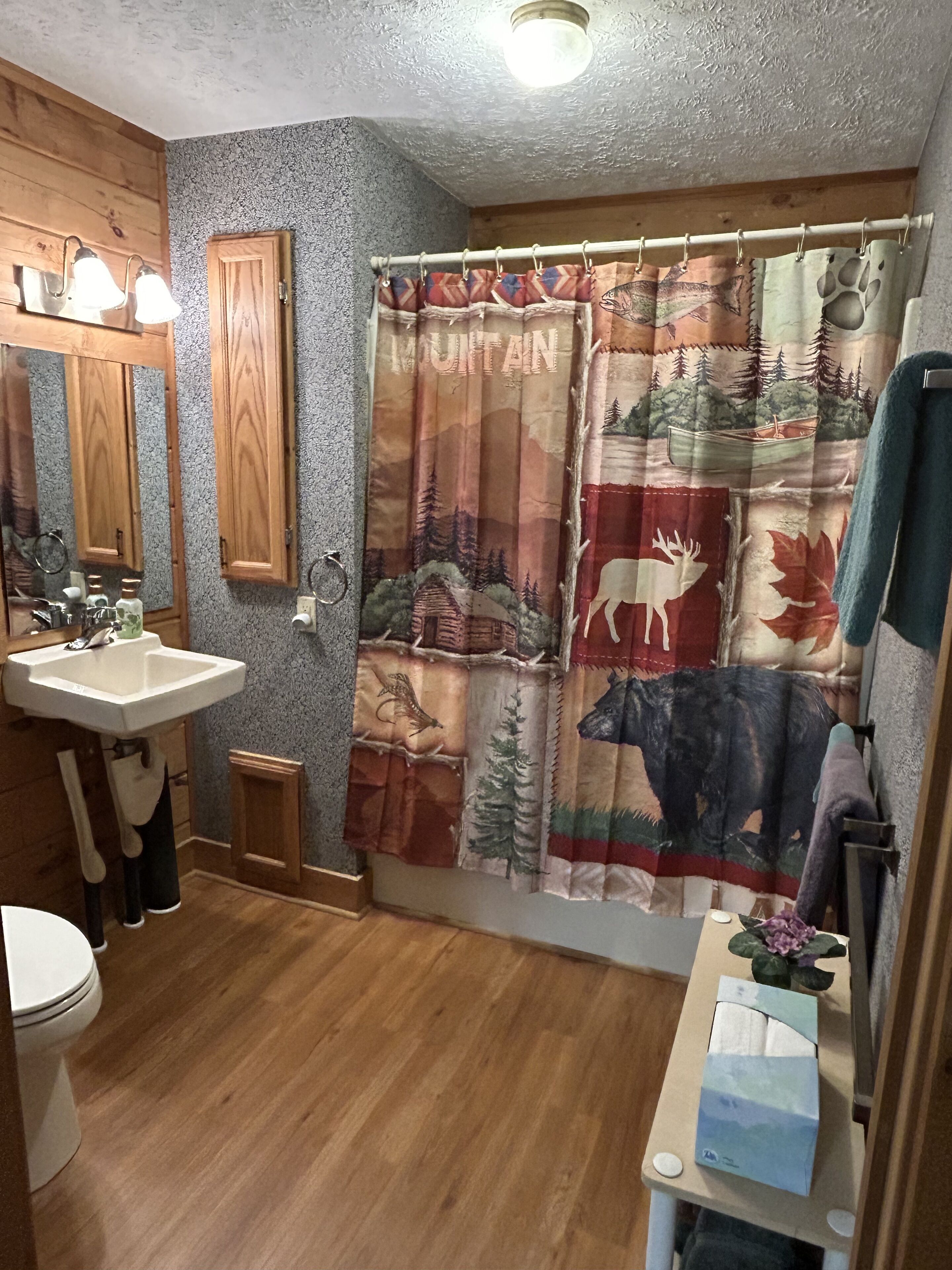 Un baño con tocador de madera, un lavamanos y una cortina de ducha con un diseño de montañas y fauna.