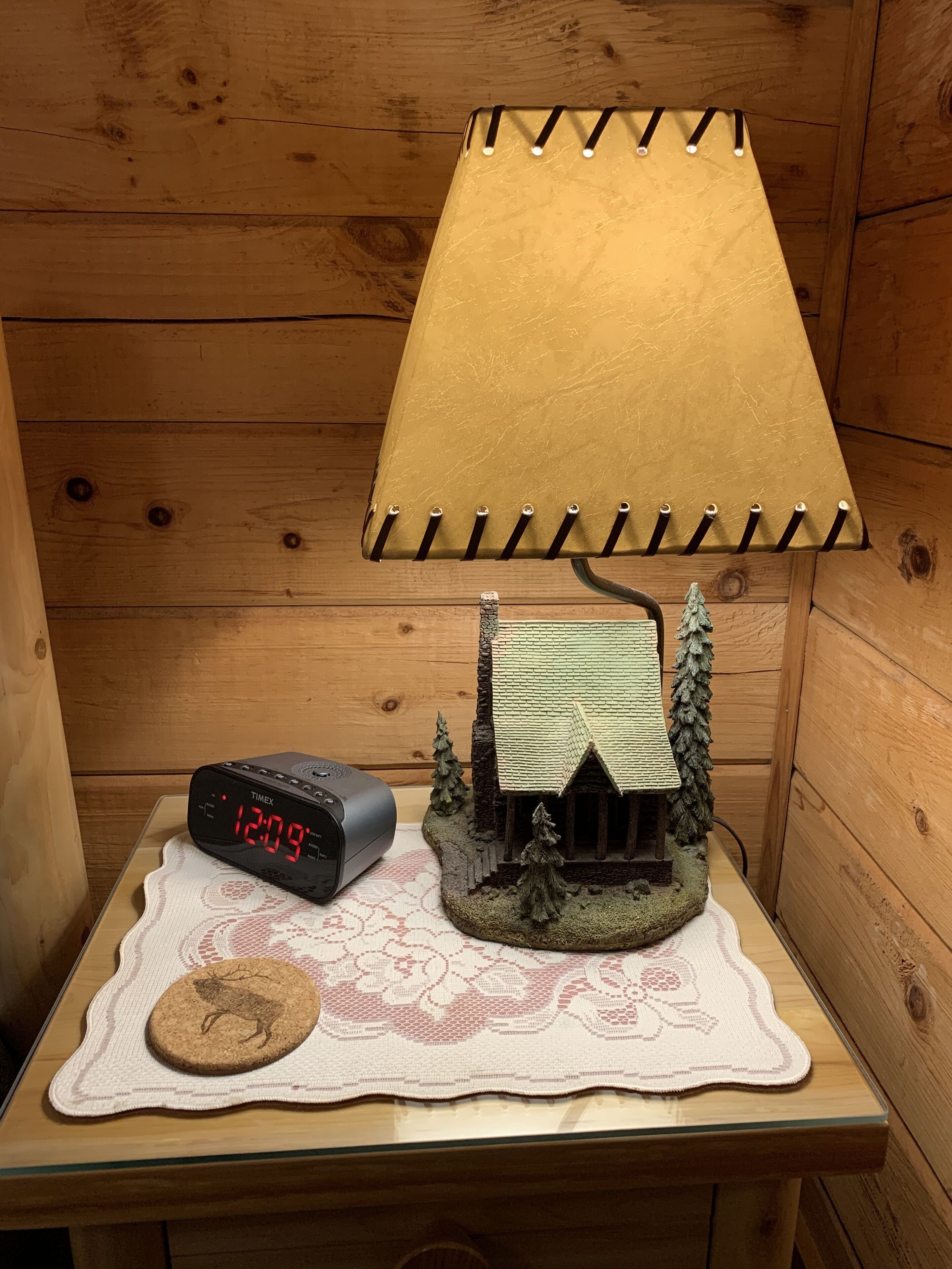 Une cabane en bois avec un petit modèle de maison, une horloge numérique et un biscuit posé sur un chemin de table en dentelle.
