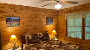 A cozy room with wooden walls, a bed with a quilt, two bedside lamps, and a ceiling fan. - Misty Creek Log Cabins (Maggie Valley)