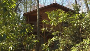 A wooden cabin with a balcony, surrounded by dense trees. - Misty Creek Log Cabins (Maggie Valley)