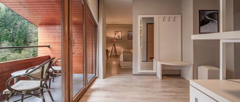 A modern interior with a wooden balcony, a dining area, and a hallway leading to a bedroom.
