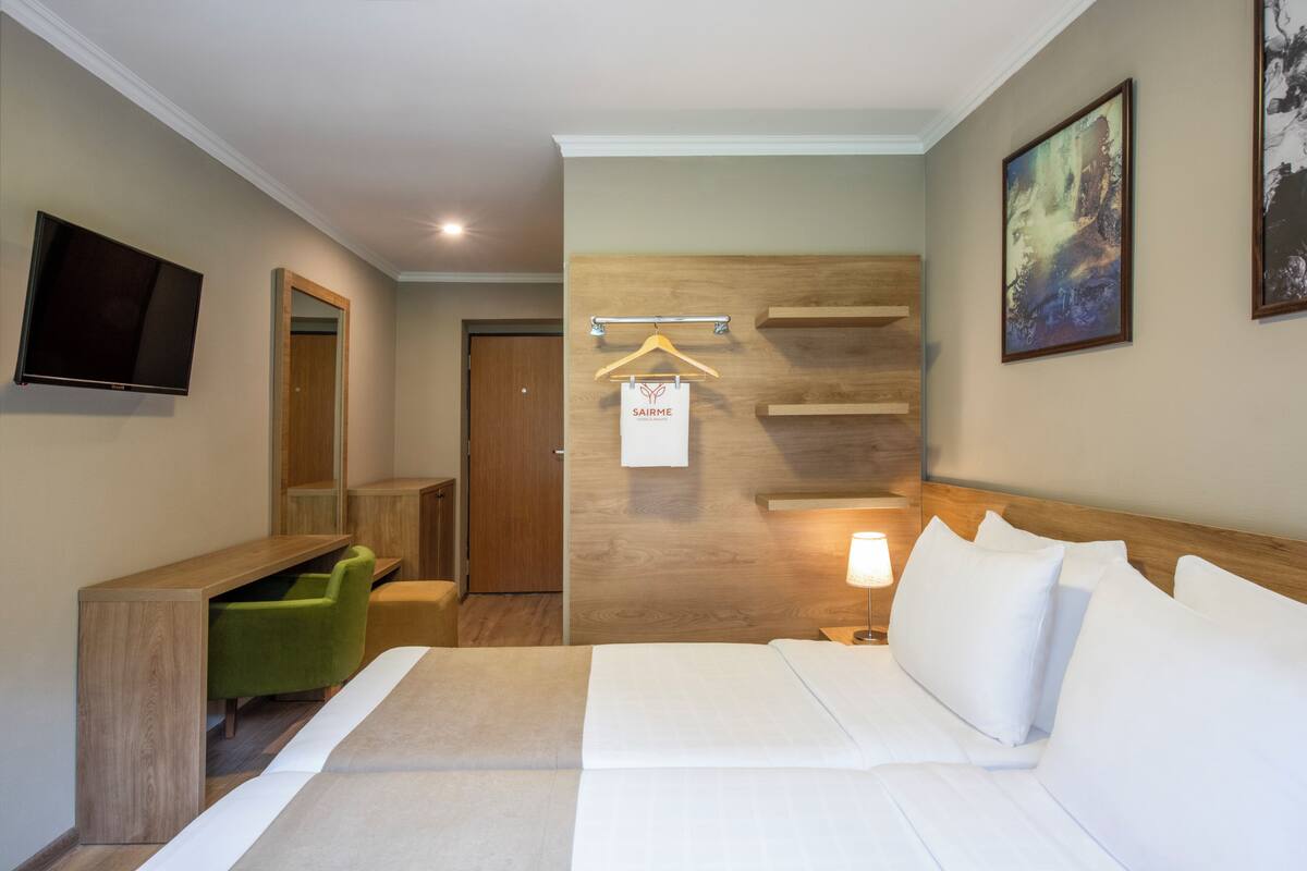 Habitación de hotel con cama, escritorio, silla, televisor, pared de madera, un cuadro y un cartel con el nombre 'SAIRME'.
