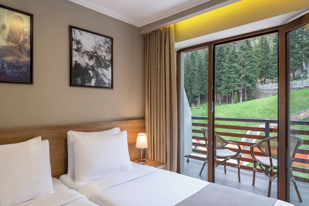 Habitación de hotel con cama, mesita de noche con lámpara y balcón con sillas.