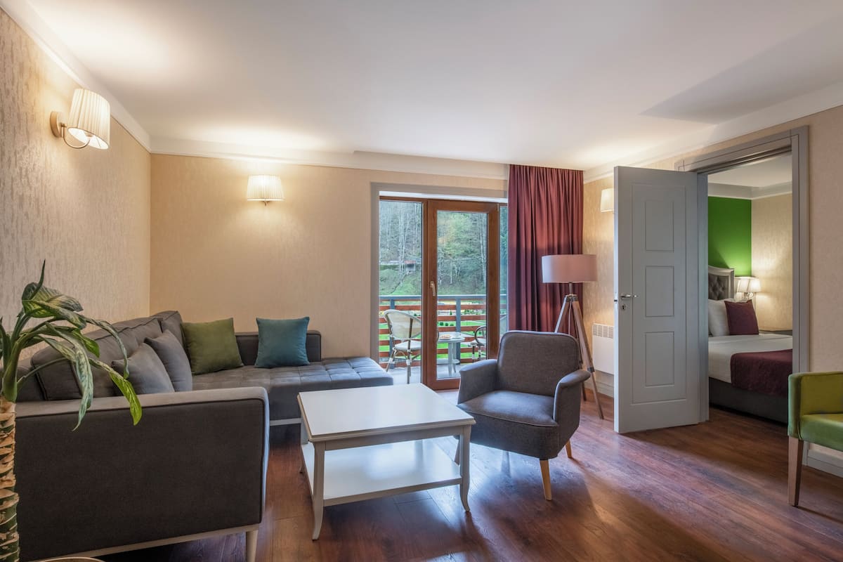 Sala de estar con sofá, sillón y mesa de centro. Hay una puerta que conduce a un dormitorio.