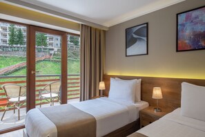 Habitación de hotel con dos camas, un balcón con sillas y vistas a un edificio y vegetación.