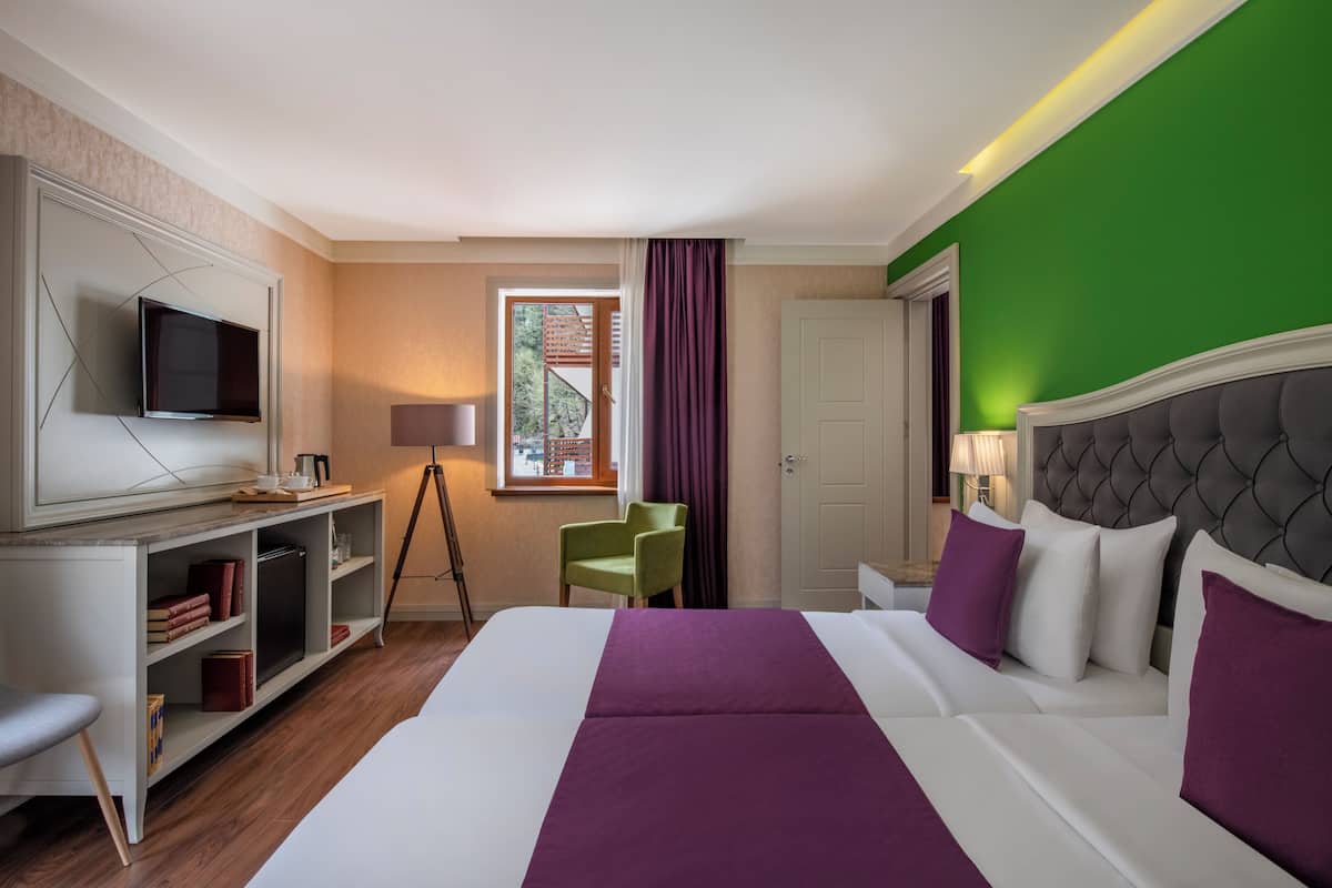 Una habitación de hotel con cama, escritorio con televisor, silla y ventana con cortinas.