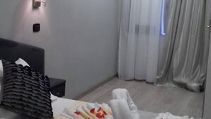 A hotel room with a neatly made bed, a bedside table, a lamp, and a window with curtains. - Hotel LePinède (Giugliano in Campania)