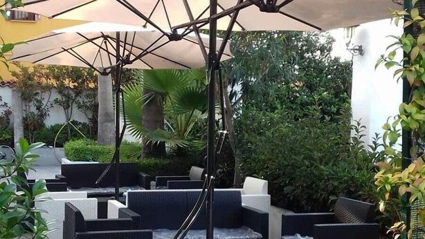 An outdoor seating area with wicker furniture, umbrellas, and greenery. - Hotel LePinède (Giugliano in Campania)