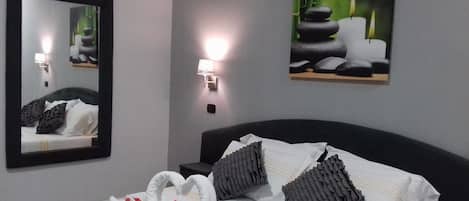 A hotel room with a bed, a mirror, wall-mounted lights, and two framed pictures.