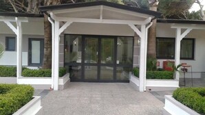A modern building entrance with a covered porch, glass doors, and white pillars. - Hotel LePinède (Giugliano in Campania)