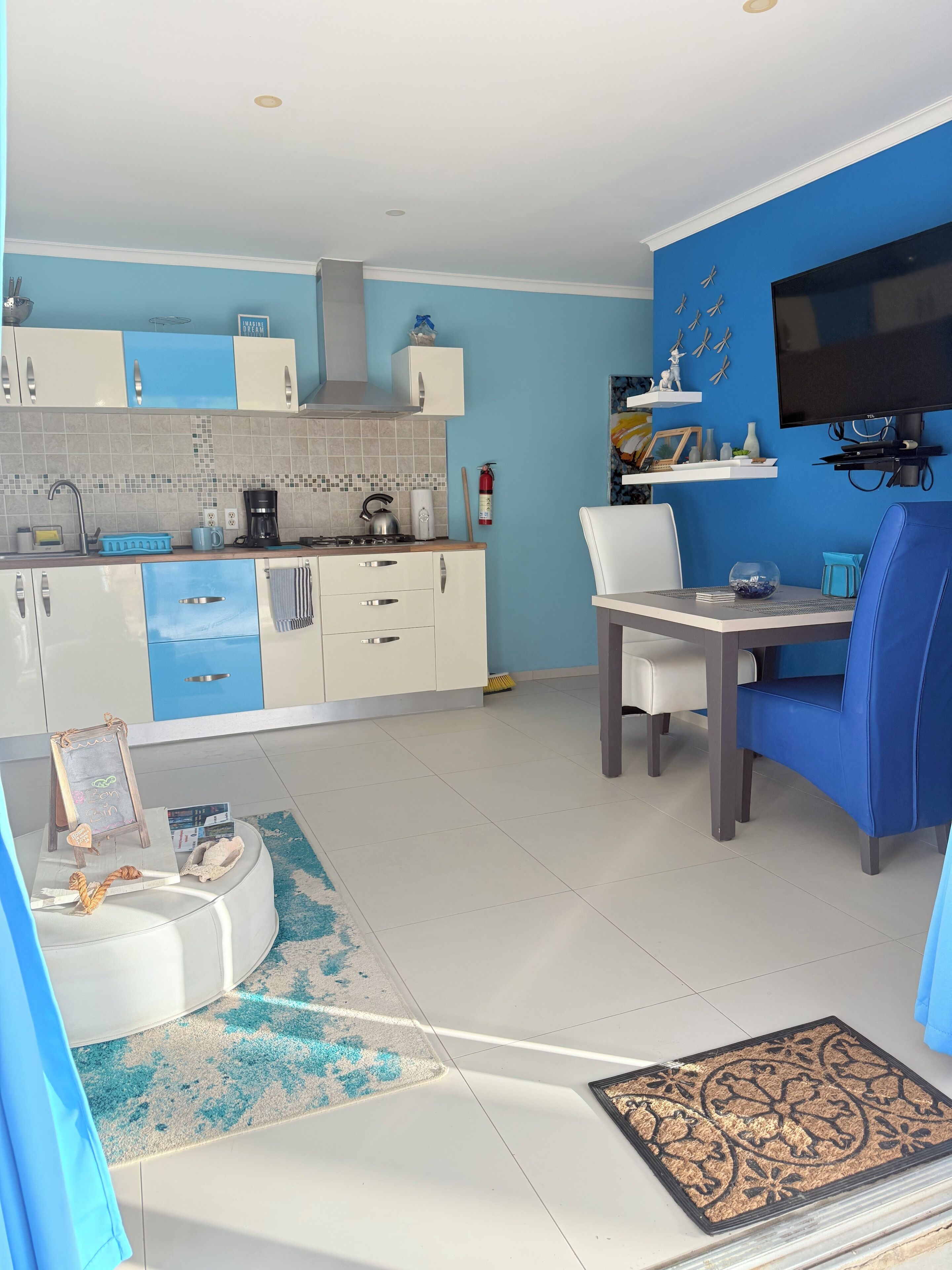A modern kitchen with white and blue cabinets, a dining area with a white table and blue chairs, and a blue accent wall.