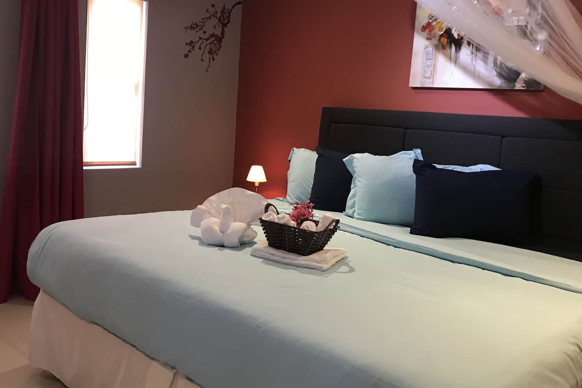 Een net opgemaakt bed met een lichtblauwe spreidek, een wit, zacht kussen, en een mand met bloemen en een handdoek.
