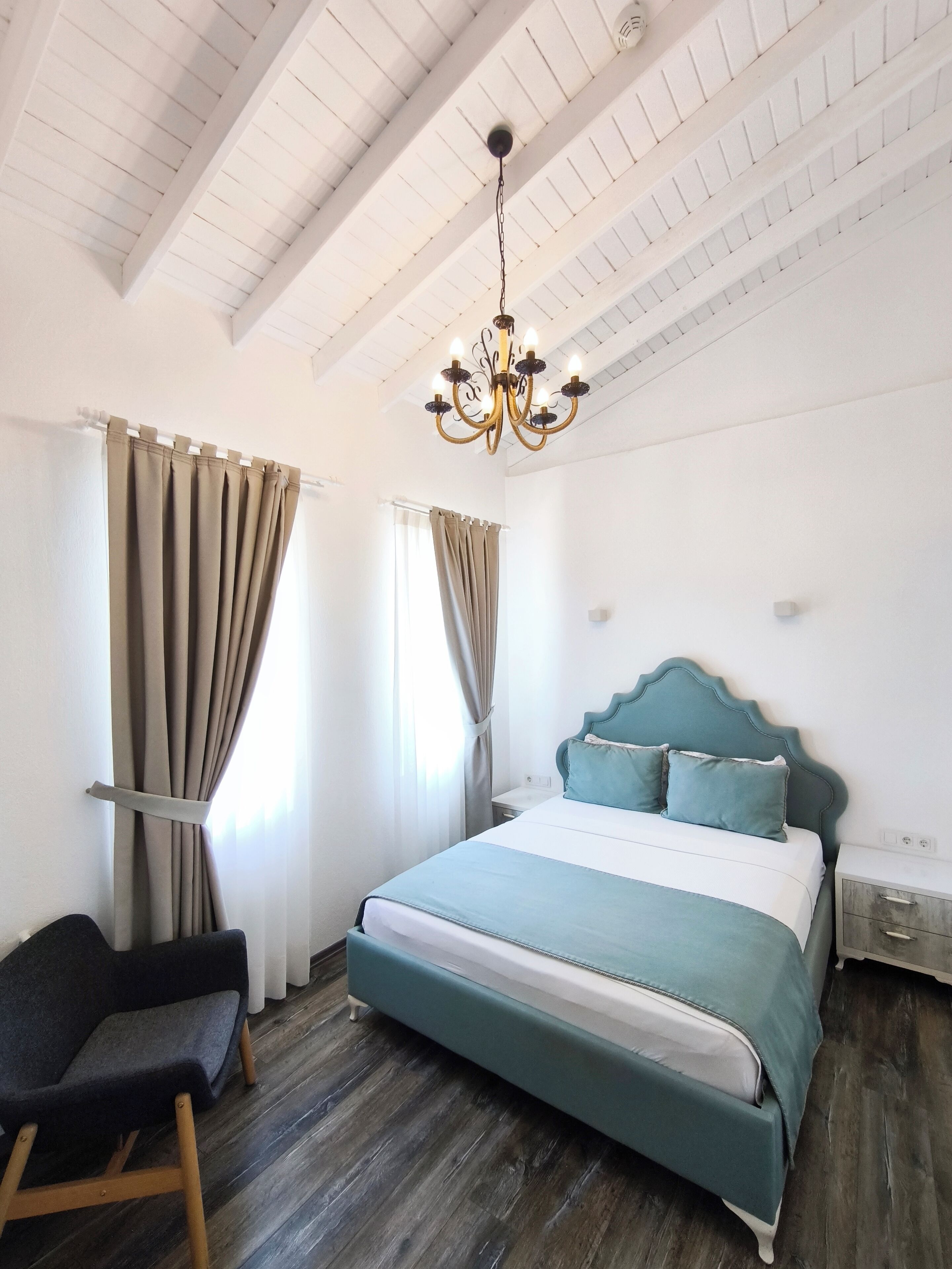 Un dormitorio con cama, una silla, una mesita de noche, un candelabro y cortinas.