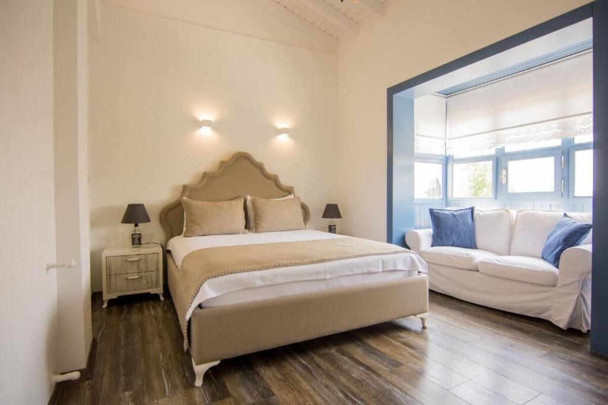 A bedroom with a bed, bedside tables, a nightstand, a sofa, and a window.