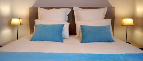 A neatly made bed with white and blue bedding, two lamps on either side, and a wooden headboard.
