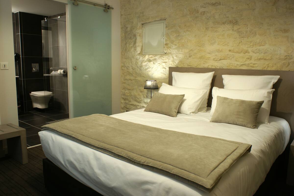 Een hotelkamer met een groot bed, een bedlamp, een stenen muur en uitzicht op de badkamer.
