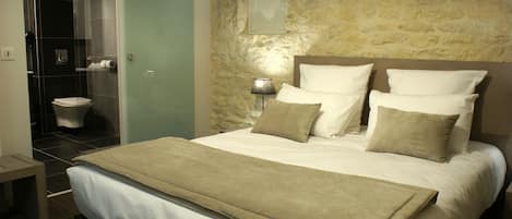 A hotel room with a large bed, a bedside lamp, a stone wall, and a view of the bathroom.