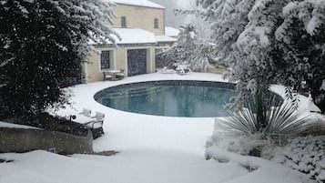 Een besneeuwde omgeving buiten met een zwembad, omringd door bomen en een gebouw.