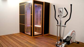 A room with a wooden floor, a sauna, and an exercise machine.