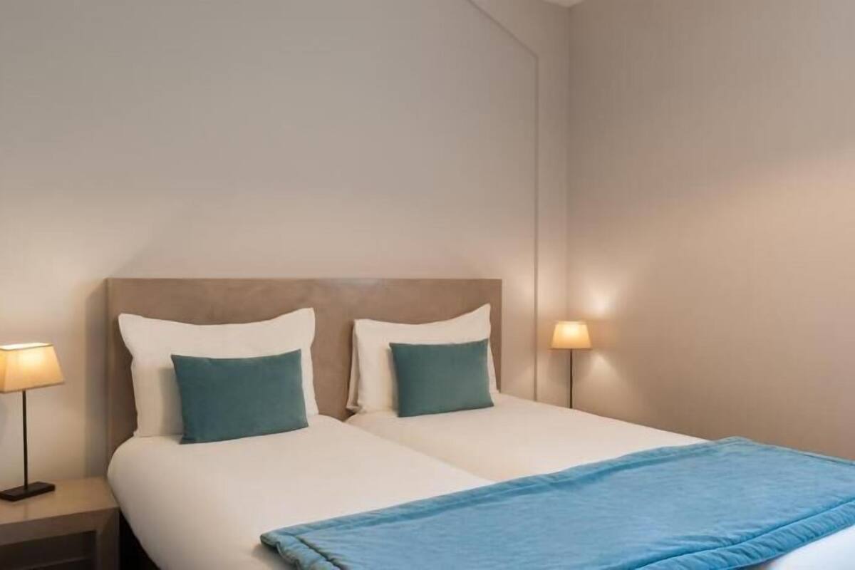 Een hotelkamer met een bed, twee bedlampen en een blauwe plaid.
