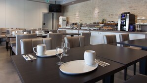 Een moderne eethoek met tafels voor twee personen, voorzien van witte borden, kopjes en bestek.