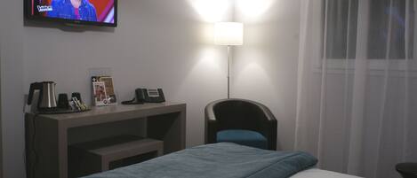 A hotel room with a bed, a desk with a telephone, a coffee maker, and a television displaying a show.