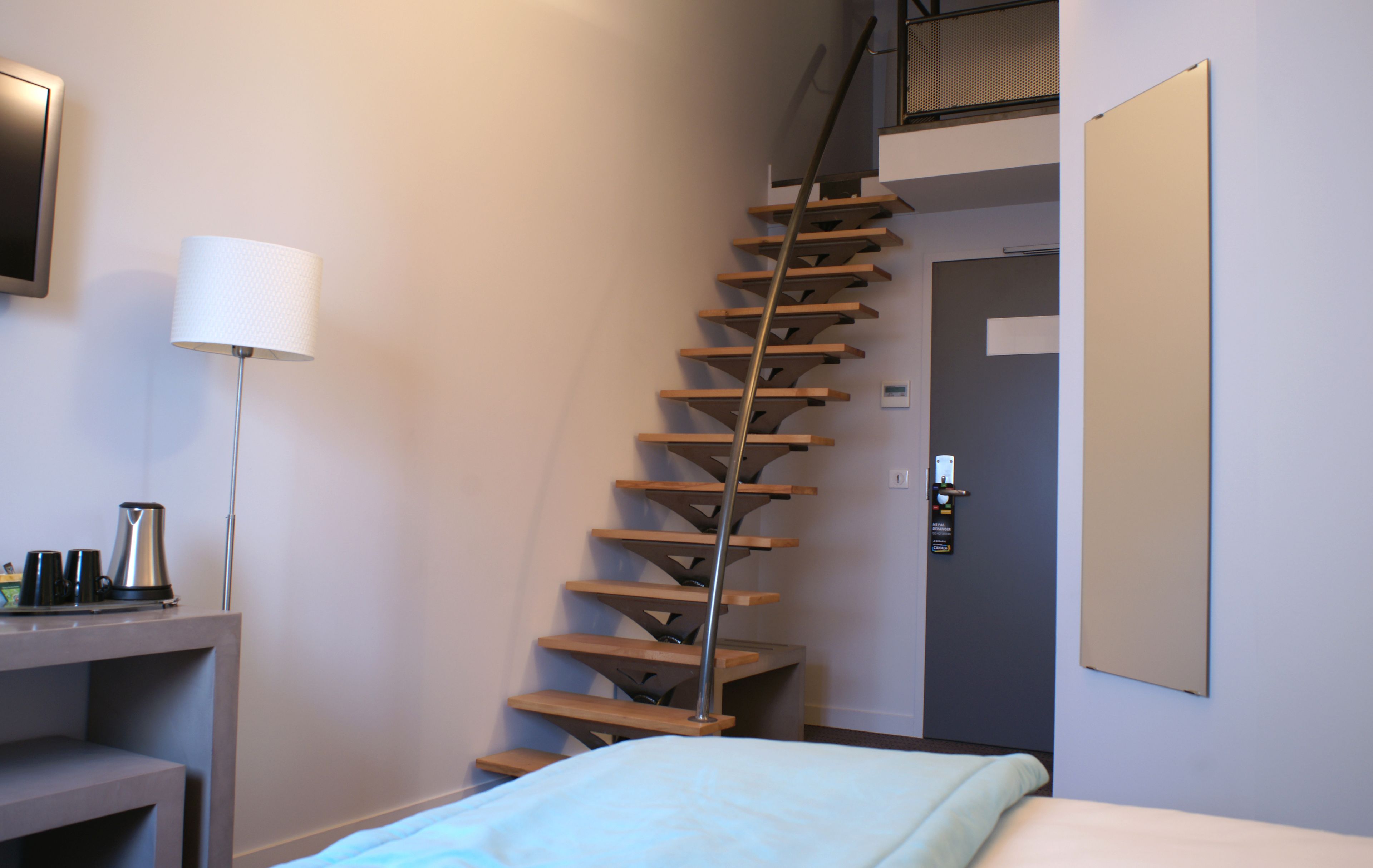 A staircase in a hotel room with a bed, a lamp, and a coffee maker on a table.