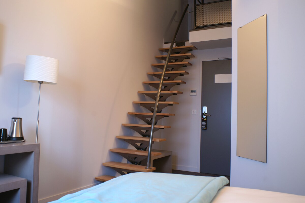 Een trap in een hotelkamer met een bed, een lamp en een koffiezetapparaat op een tafeltje.