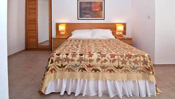A hotel room with a bed, a nightstand, a wall-mounted lamp, and a painting above the bed.