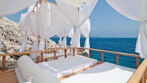 A wooden deck with white beds and canopy tents overlooking a rocky coastline and the sea. - Lycia Hotel (Kas)