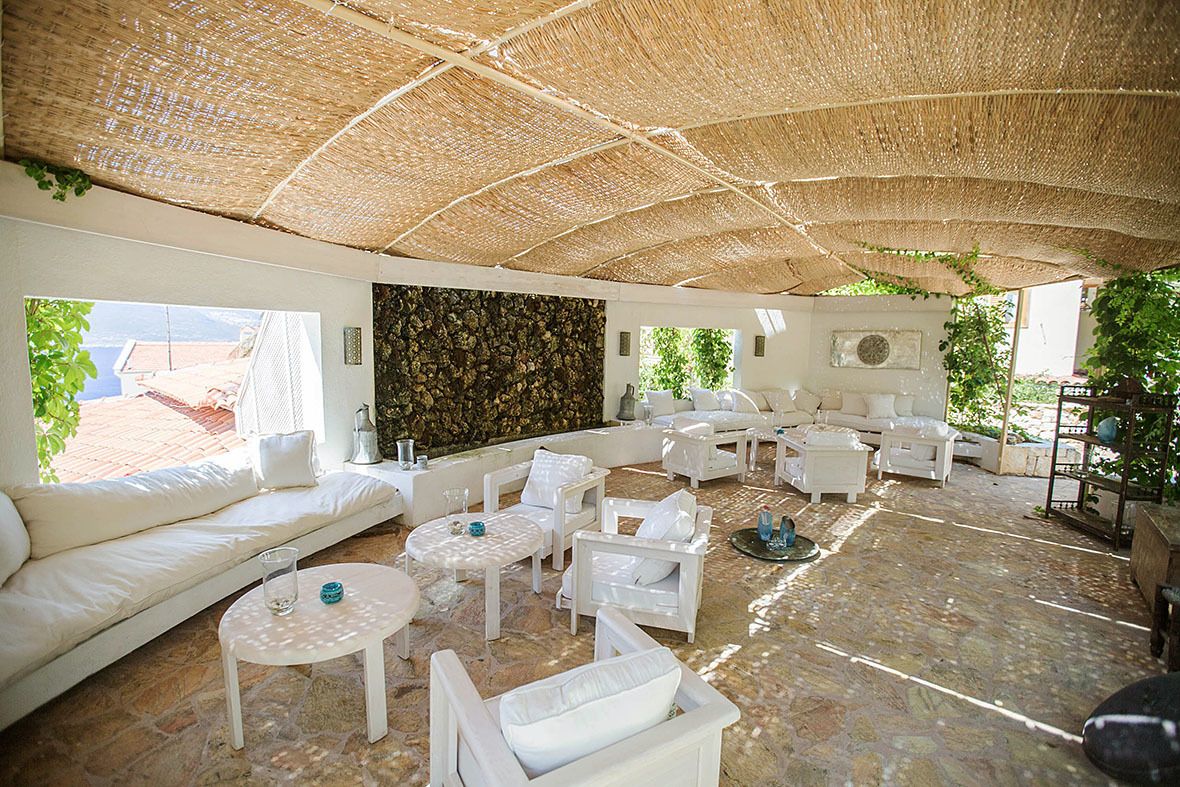 A spacious outdoor lounge area with white furniture, a stone wall, and a thatched roof.