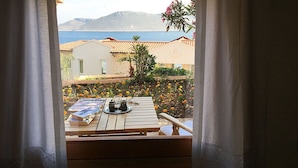 A view from a window with curtains, overlooking a patio area with a wooden table, a book, and a teapot. - Lycia Hotel (Kas)