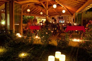 An outdoor dining area with wooden beams and tables set for a meal, surrounded by greenery and flowers. - Lycia Hotel (Kas)