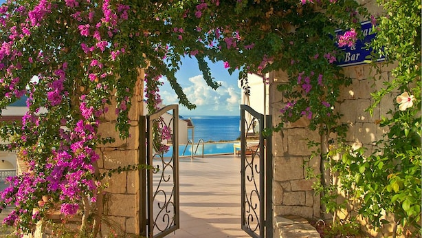 A stone gate with a blue sign reading "Bar" leading to a pool area with a view of the sea. - Lycia Hotel (Kas)