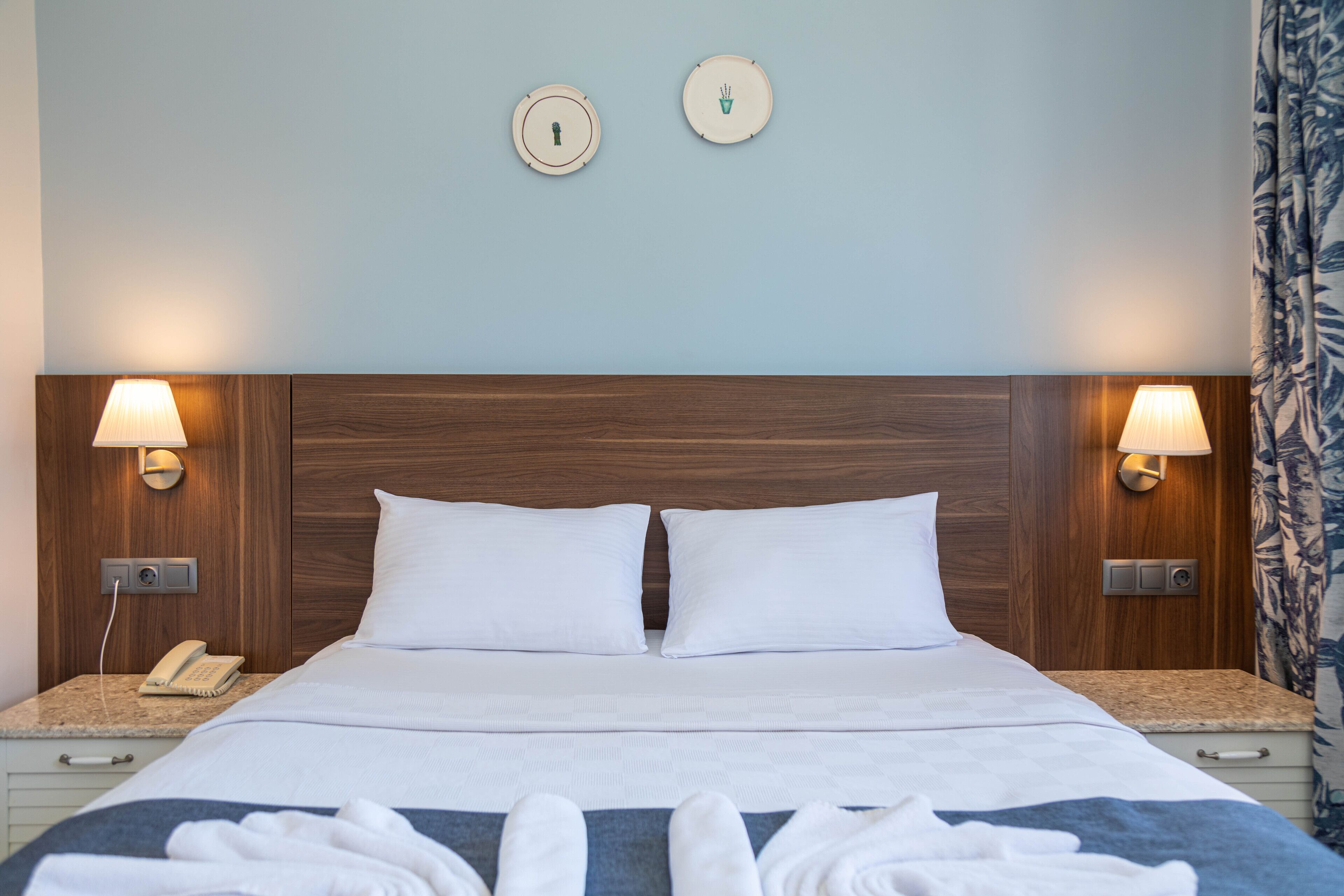 Habitación de hotel con cabecera de madera, dos lámparas de noche, un teléfono y una cama bien hecha con toallas.