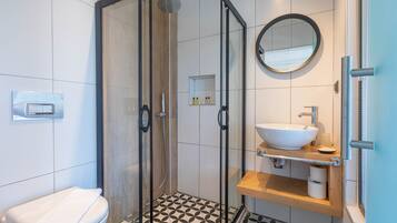 A modern bathroom with a glass-enclosed shower, a white sink, and a wooden vanity.