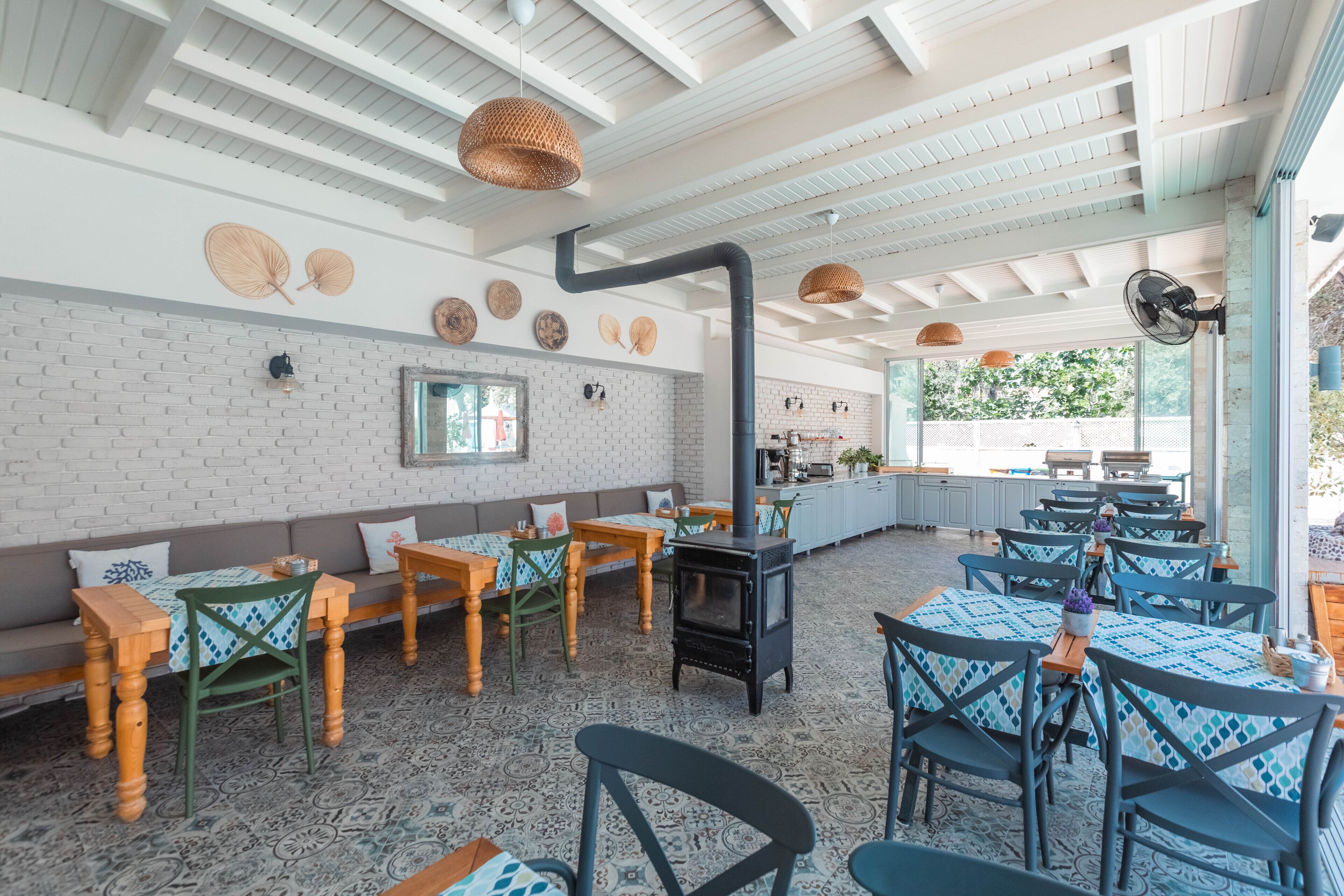 A restaurant with a brick wall, wooden tables, and chairs, a black stove, and hanging baskets.