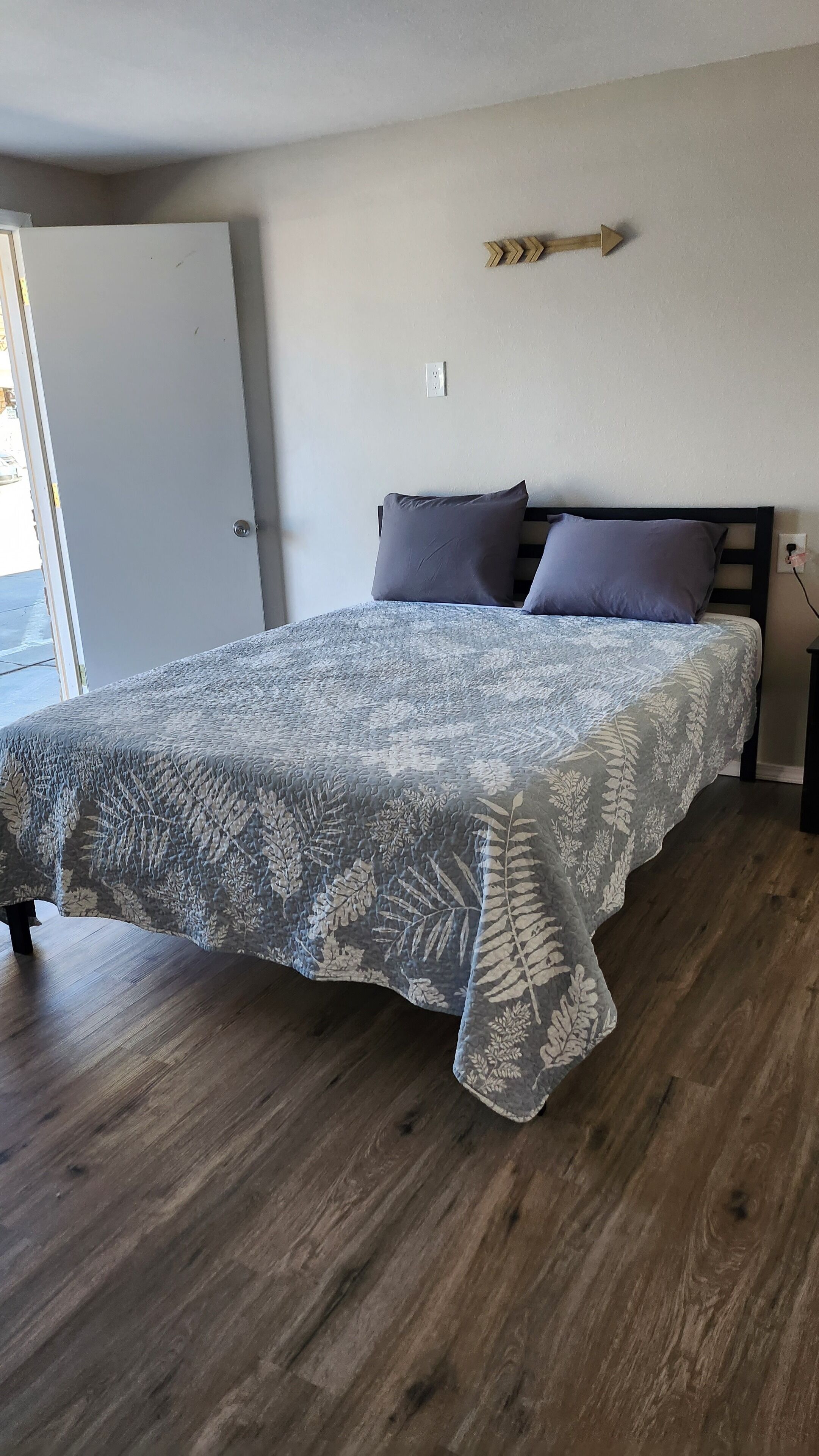 A bedroom with a bed, a wooden headboard, a nightstand, and a door.