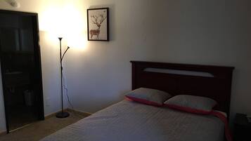 A bedroom with a bed, a nightstand, a lamp, a framed picture on the wall, and a door to a bathroom.