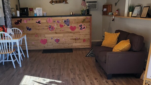 A cozy interior with a wooden reception desk, a sofa with yellow cushions, and a dining area with white chairs. - Golden Arrow Motel (Lamar)