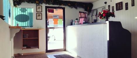 A reception area with a desk, a bookshelf, and a door leading outside.