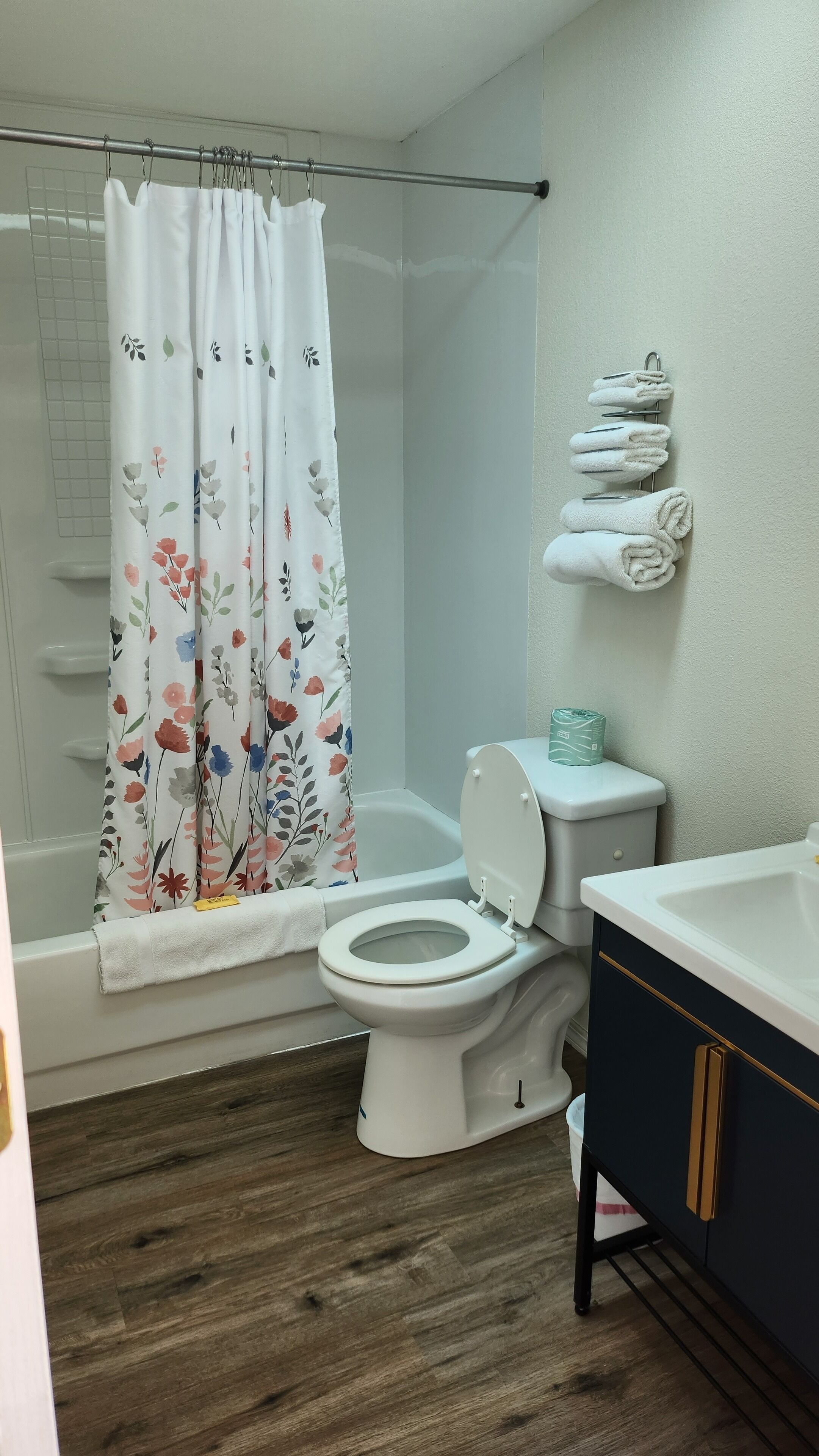 Un baño con inodoro, cortina de ducha con motivos florales, bañera y lavamanos con toallas.