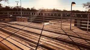 A wooden deck with a metal railing, a street lamp, and a sign in the background. - Golden Arrow Motel (Lamar)