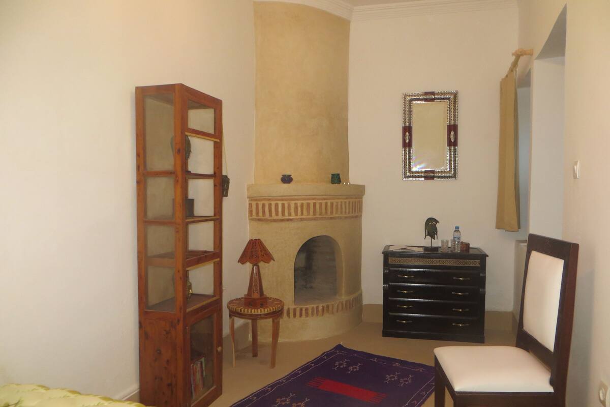 A bedroom with a bed, a dresser, a mirror, a fireplace, and a bookshelf.
