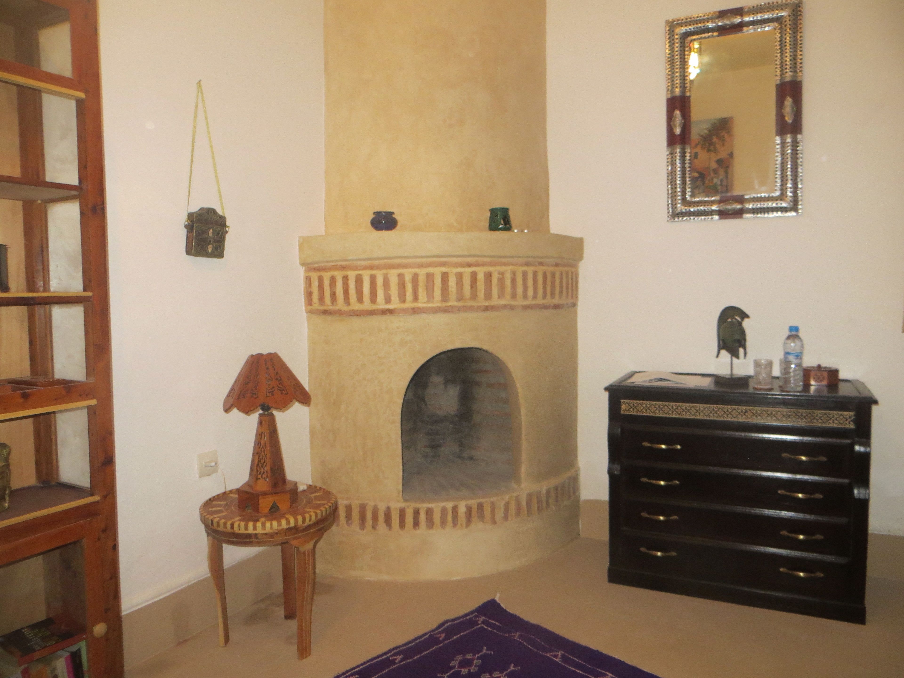Um quarto com lareira, um espelho, um armário de madeira e uma pequena mesa com abajur.