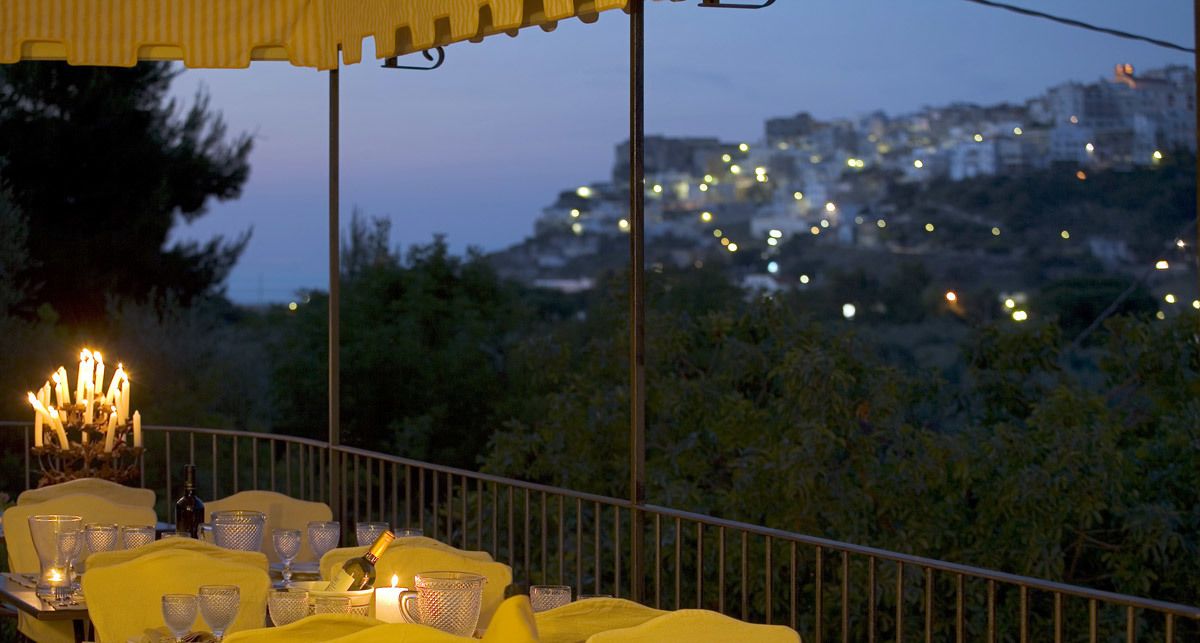 Un espace de restauration en plein air avec des chaises et des tables jaunes, un centre de table composé de bougies et une vue sur le paysage urbain au crépuscule.