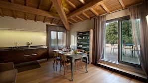 A modern kitchen with wooden beams, a dining area with a table and chairs, and a view of the outdoors through large windows. - Poste del Chiugi (Castiglione del Lago)
