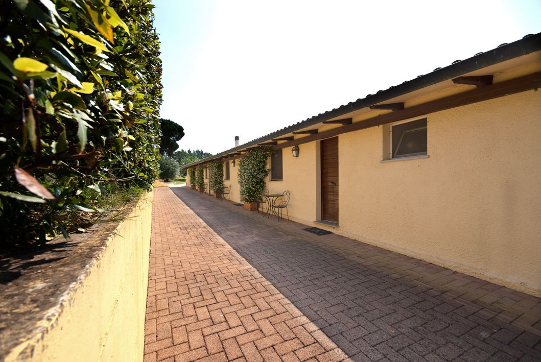 Un vialetto lastricato che conduce a un edificio con tetto in tegole e parete esterna gialla.