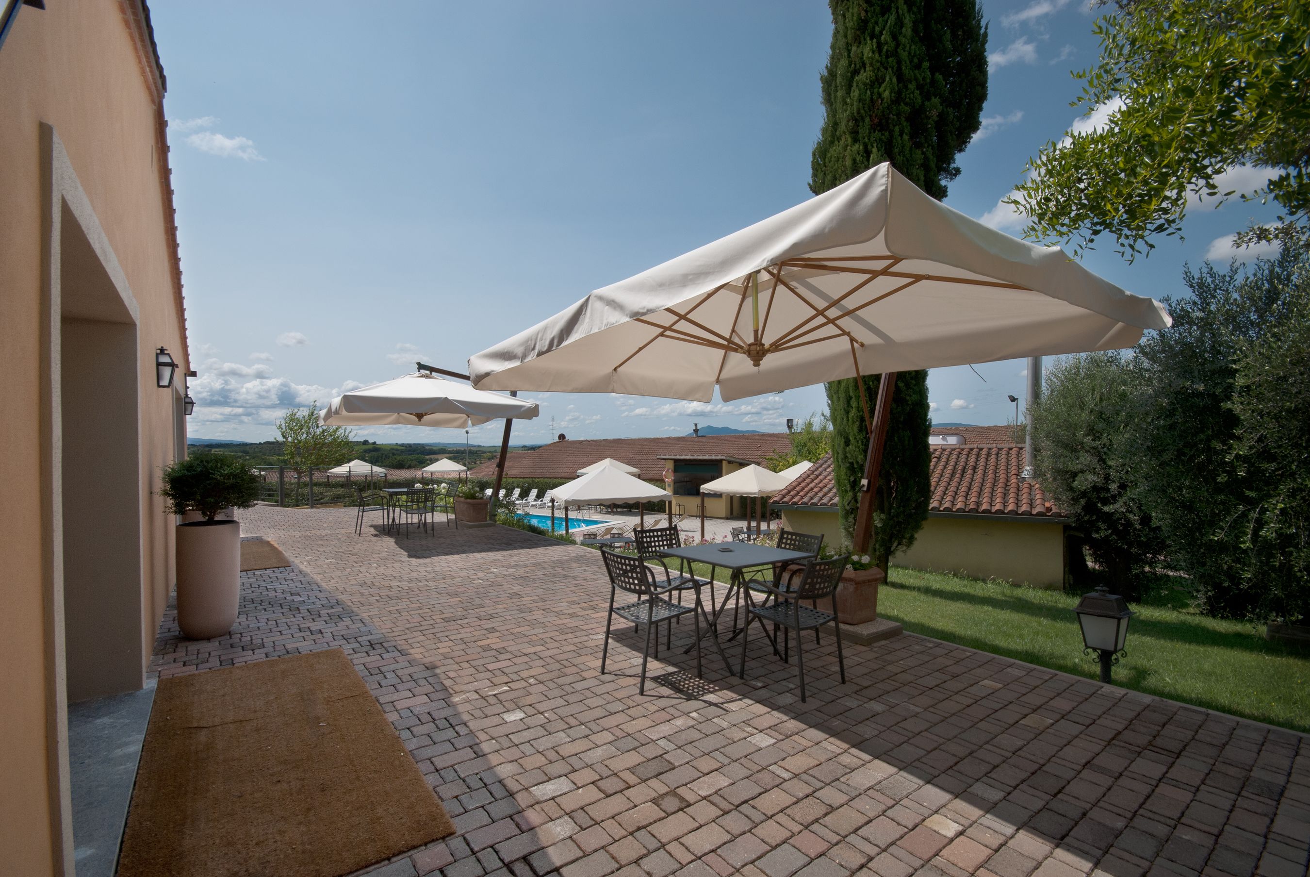 A patio area with outdoor seating and umbrellas, a swimming pool in the background, and a view of the landscape.