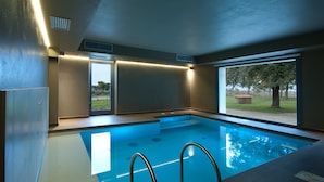 A modern indoor swimming pool with clear glass walls, a built-in ladder, and a view of the outdoors. - Poste del Chiugi (Castiglione del Lago)